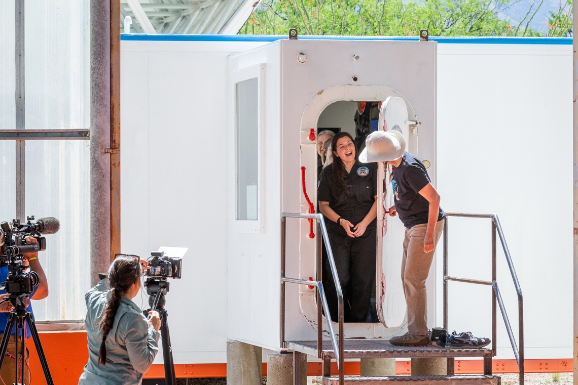 A person emerges from a hatch and is greeted by another standing outside A person emerges from a hatch and is greeted by another standing outside