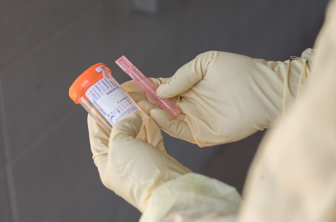 gloved hands holding a swish-gargle COVID-19 test collection kit
