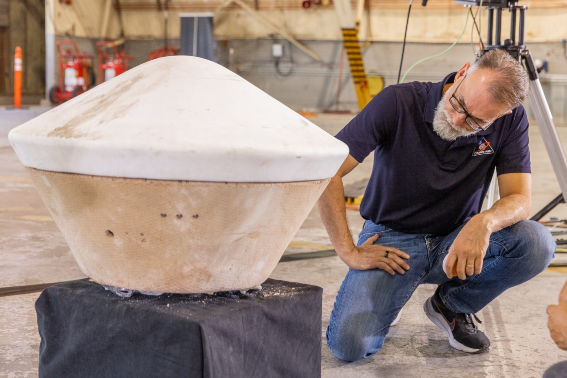 A man crouches next to a replica of the flying saucer-like sample capsule.