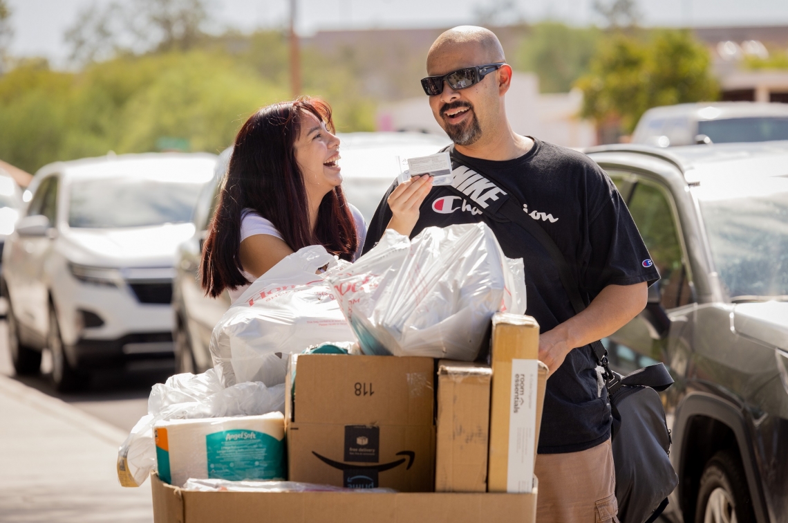 Amarissa Carabajal and her father, Moises University of Arizona student and her father laughing as they push a bin full of belongings towards a dorm room