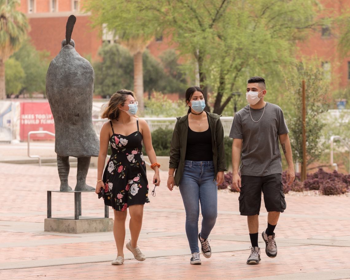 three students wearing face coverings walking on campus