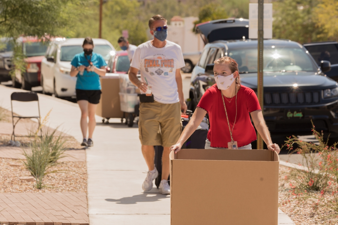 mask-wearing student with a large cardboard box moving into the dorm
