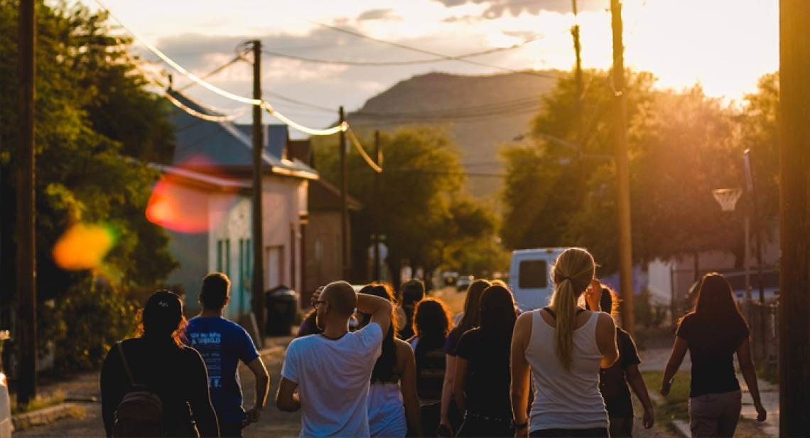 a group of people walking down the street toward a setting sun