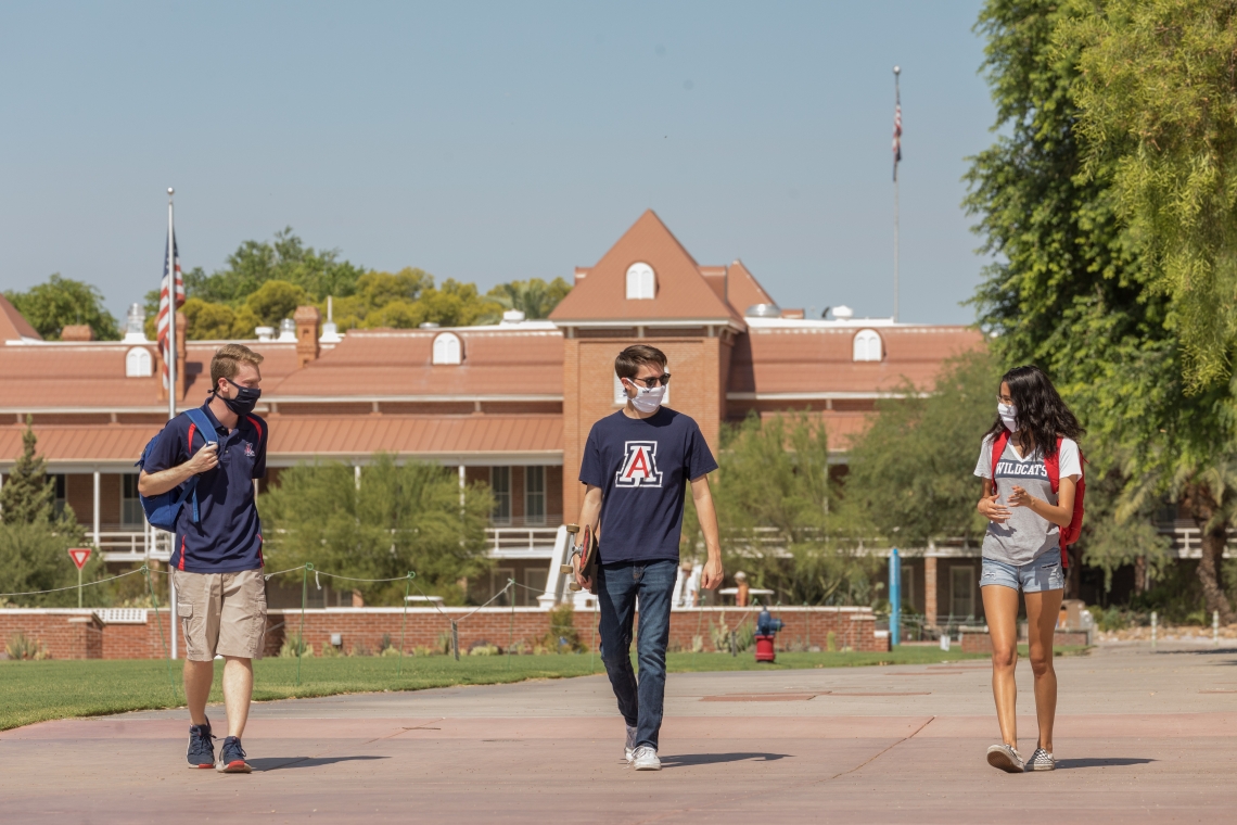 three students wearing face coverings walking in front of Old Main