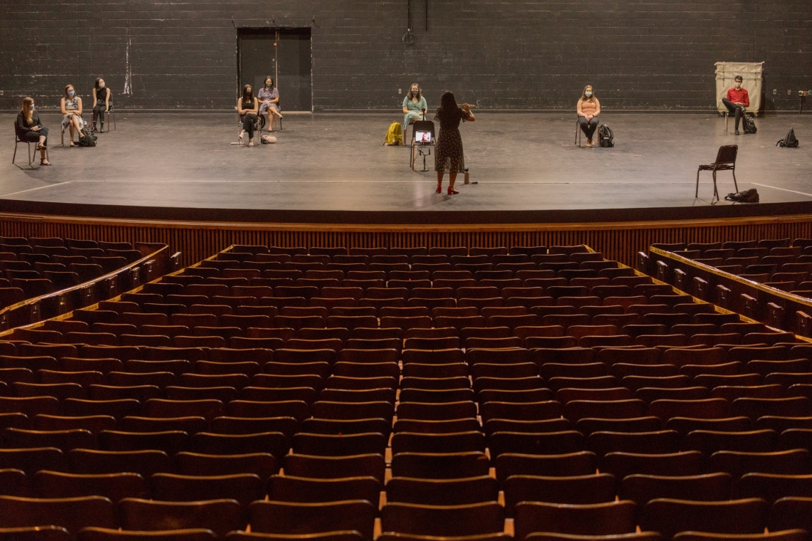 a woman plays a flut on stage in front of socially distanced students wearing masks