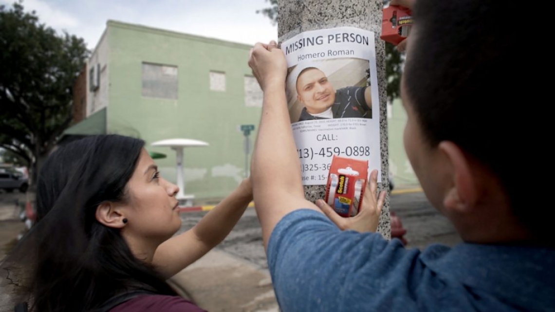 two people hanging up a sign for a missing person