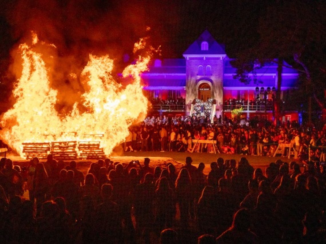 hundreds of people around a large bonfire in the evening