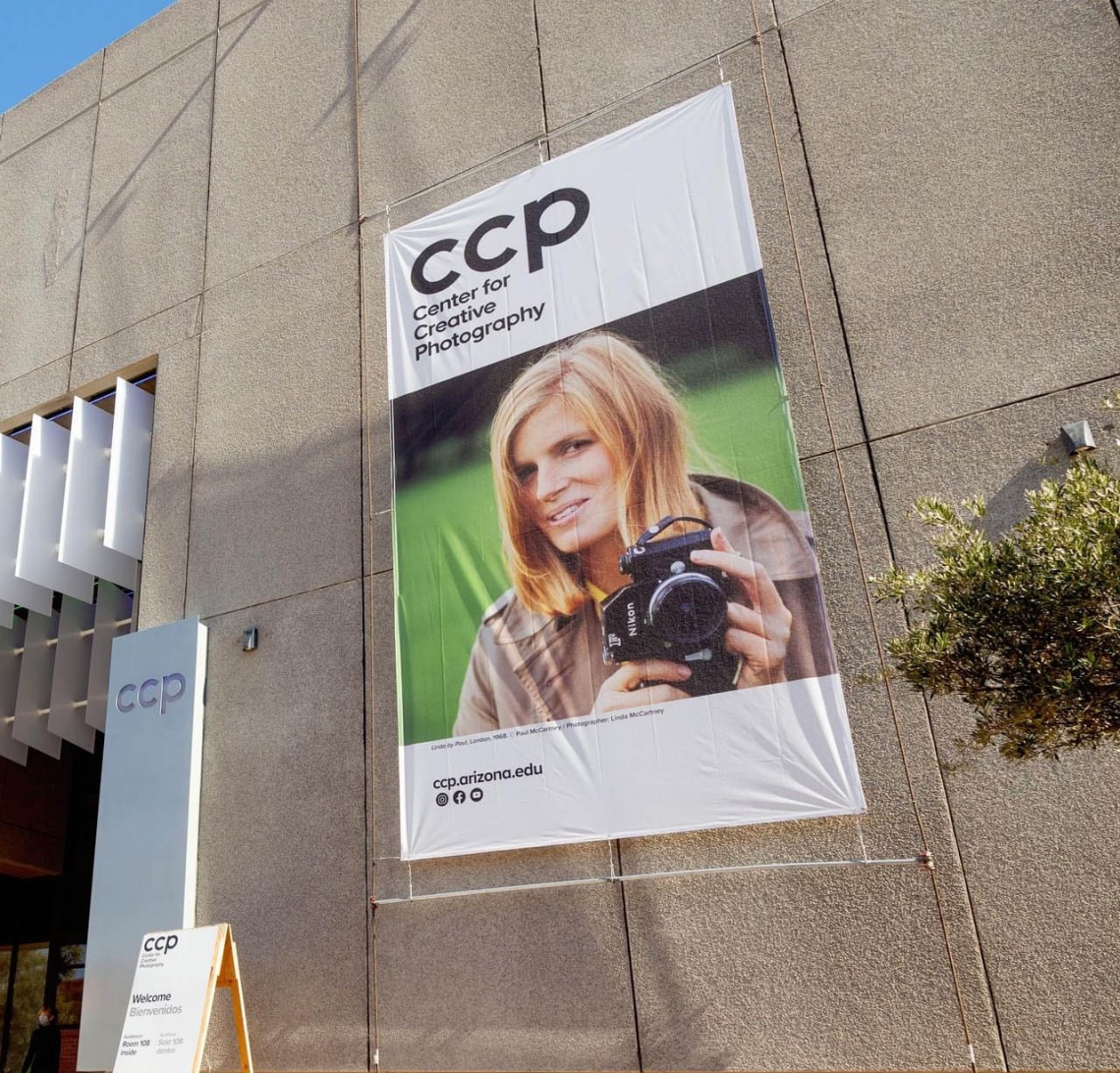 Poster for the McCartney exhibit which shows Linda McCartney taking a photograph.