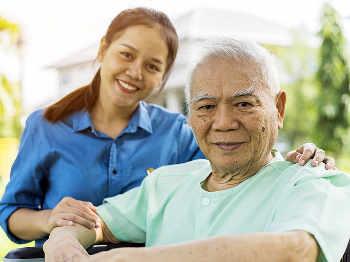 Smiling woman kneels next to smiling older man in wheelchair.