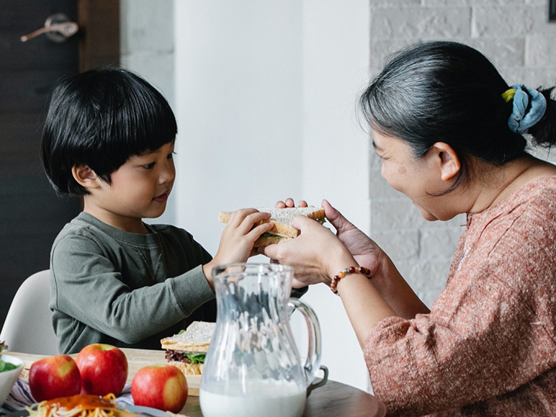 An older woman offers a sandwich to a young child