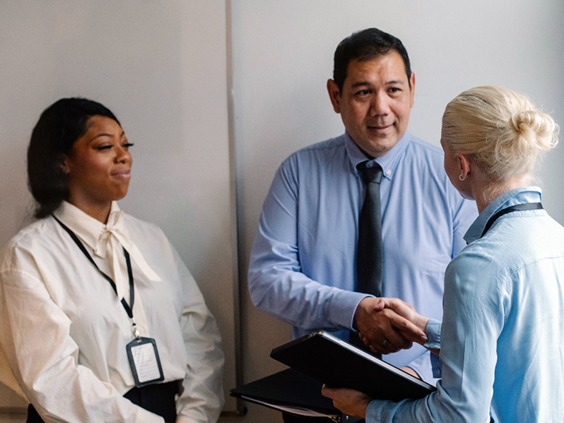 Three colleagues shaking hands in a hallway