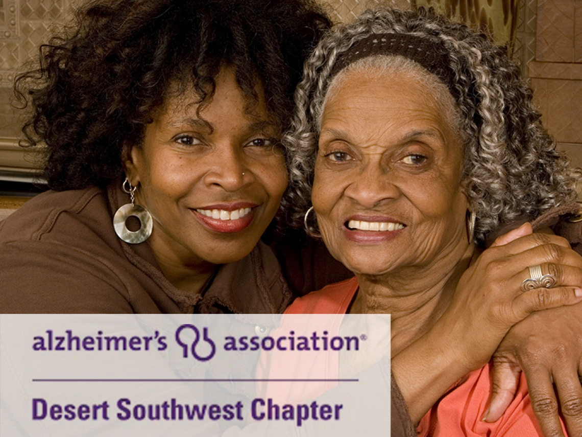 Adult woman sitting on a couch hugging her mother. Alzheimer's Association logo in corner.