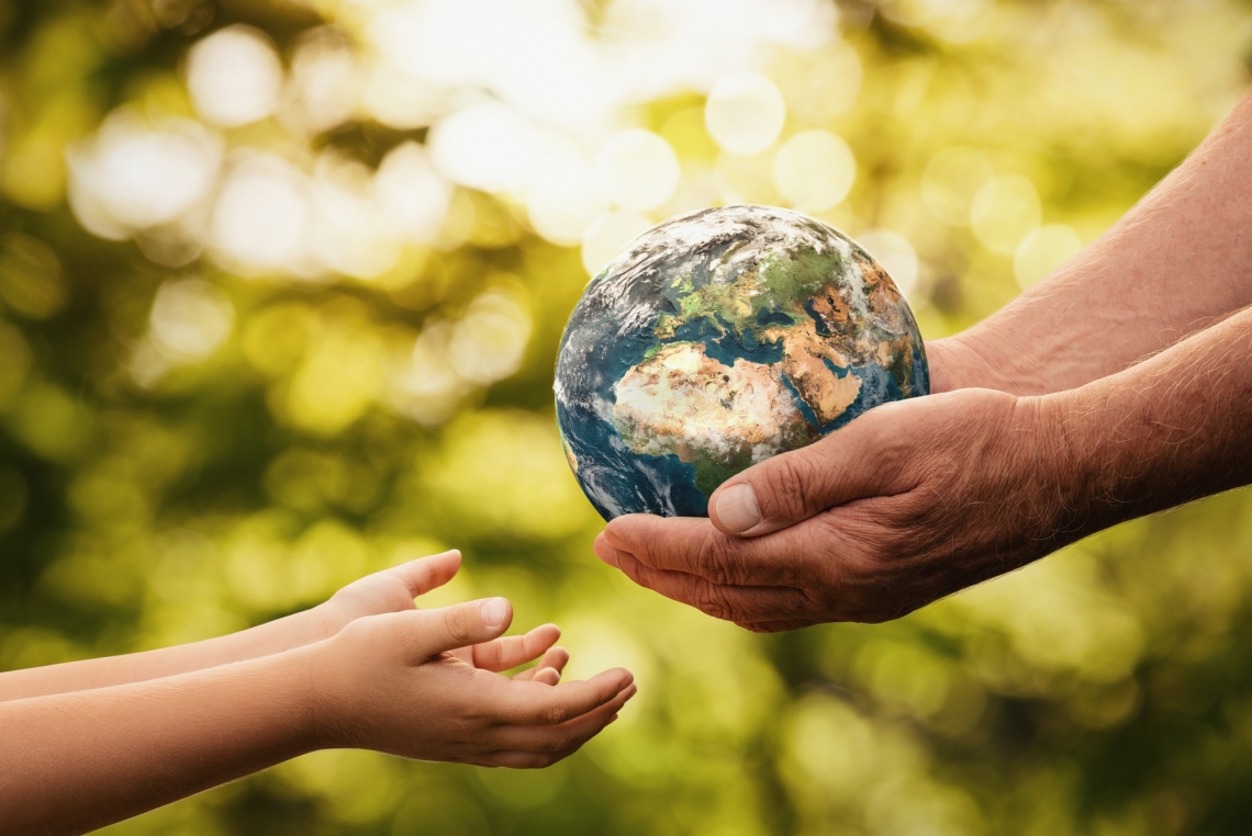 adult hands passing a small replica of Earth into a child's hands