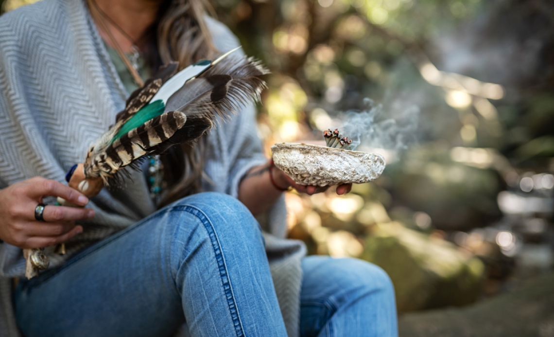 two hands holding a feather and a bowl during a smudging ceremony