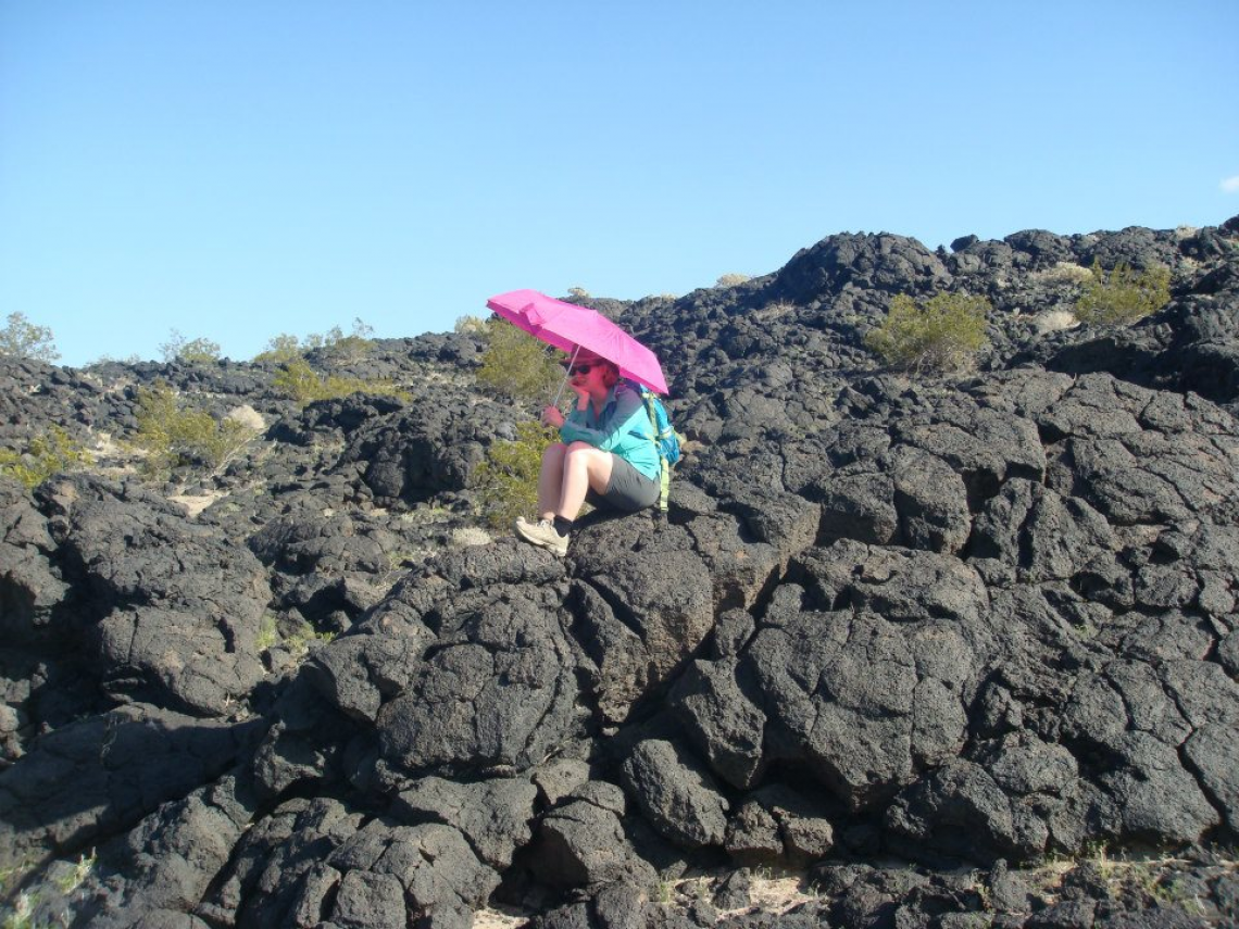 A University of Arizona Lunar and Planetary Laboratory student holds a bright umbrella over the spot where she found geologic contact between two different lava flows during a trip to Amboy Crater in California's Mojave Desert.  