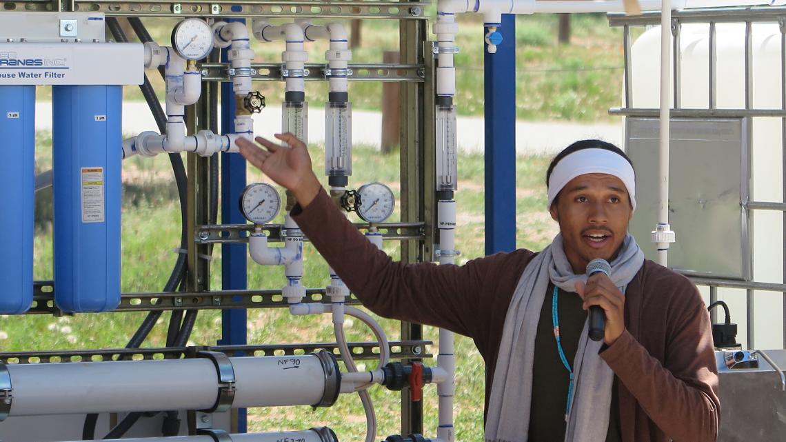 Diné College student and Indige-FEWSS participant Larry Moore demonstrates use of the solar-powered water filtration system to community members on Navajo Nation.