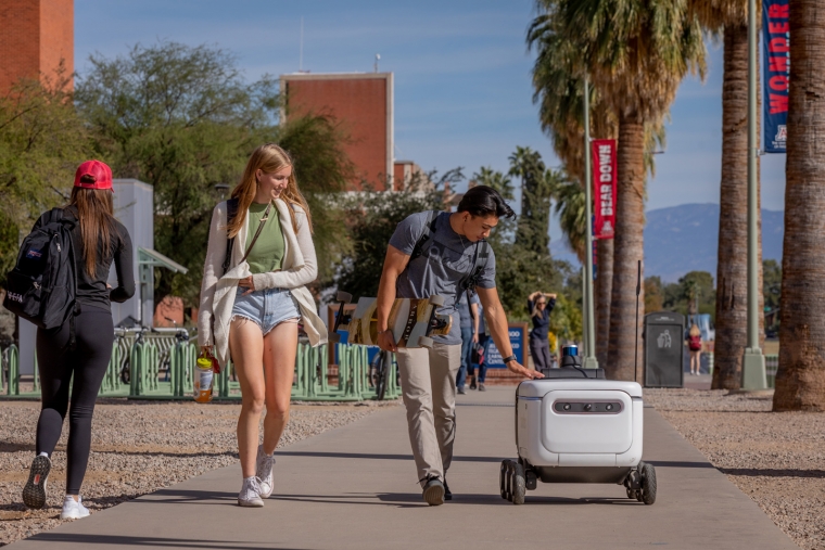 A student pets a passing food delivery robot on campus A student pets a passing food delivery robot on campus