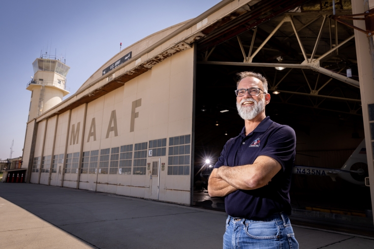 A smiling man in front of an army hangar