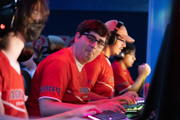 A man in a red shirt looks towards the camera while frowning