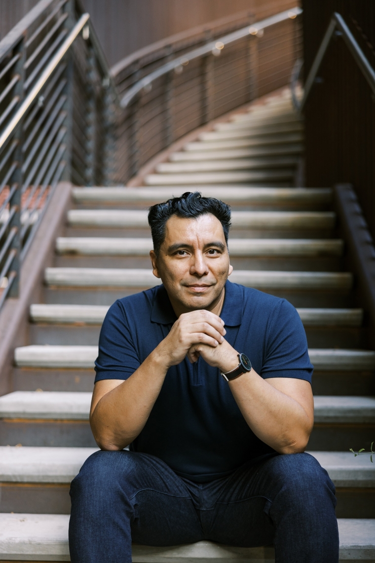 University of Arizona professor of English Manuel Muñoz A man in a blue shirt sits at the bottom of a staircase with his elbows on his knees