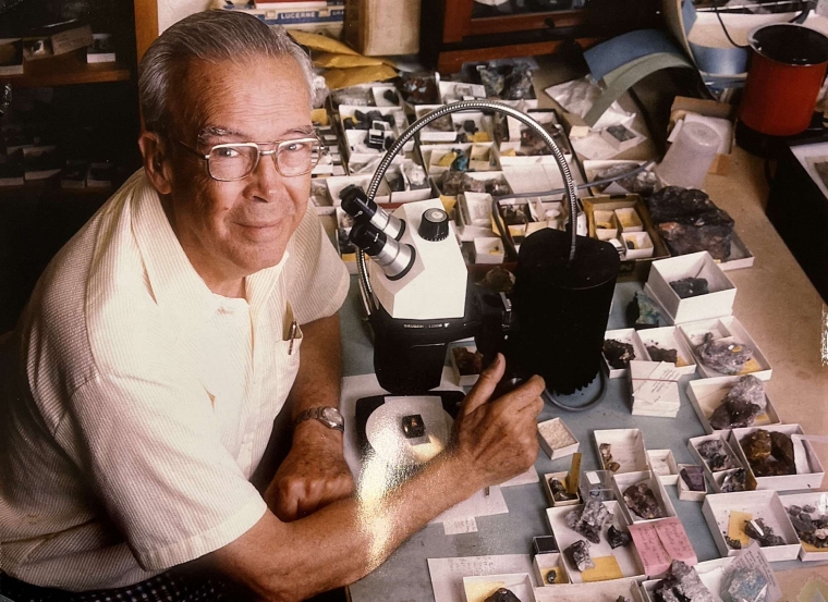 Arthur Roe sitting at a desk full of boxes of small minerals