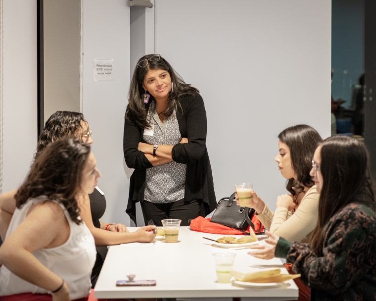 Gloria Montaño Greene standing near a table listening to students talking
