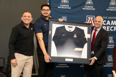 three men, two of which are holding a framed rugby jersey