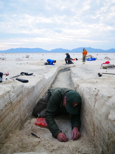 Archaeologists dig in a trench in the flat white sand