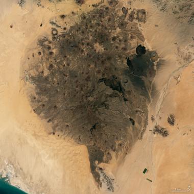 The volcanic cinder cone field of the Pinacate Peaks stands out against the surrounding sand dunes. 